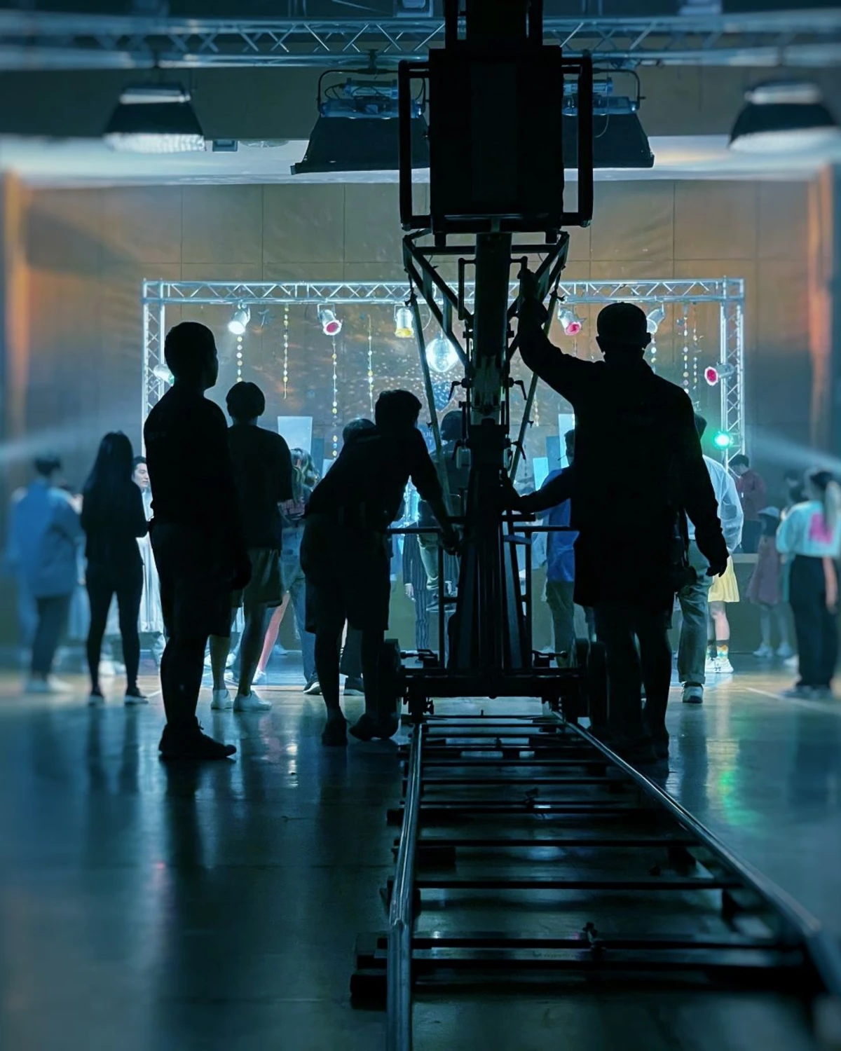 A camera dolly on tracks aimed at a brightly lit set with silhouetted crew in the foreground
